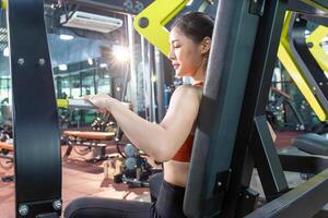 asiatique femme travail en dehors dans le salle de sport, Jeune aptitude femmes exécuter exercice avec machine d'exercice physique dans le Gym photo