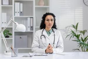 professionnel hispanique femelle médecin engagé dans une appel avec une patient, Parlant directement de sa clinique bureau. photo