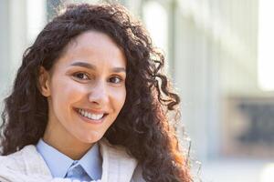 fermer portrait de content magnifique hispanique femelle Bureau ouvrier permanent à l'extérieur Bureau dans soleil, incroyable brunette étudiant à la recherche avec contentement à caméra et souriant. photo