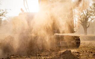 Tractopelle travail par creusement sol à construction placer. excavatrice travail sur démolition site avec poussière dans le air. fouille machine. Terre en mouvement machine. les fouilles véhicule. construction entreprise. photo