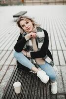 femme avec blanc écharpe profiter café sur banc. détendu femme séance sur banc, enveloppé dans une confortable blanc foulard, en portant une tasse, profiter une serein moment en plein air. chaud et attrayant atmosphère. photo