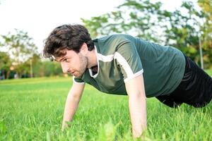 Jeune homme avec vert T-shirt Faire des pompes concentré dans parc photo