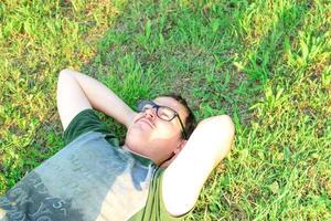 Jeune homme avec des lunettes menti sur herbe profiter vacances après en train d'étudier très content photo