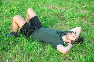 Jeune homme avec vert T-shirt mensonge détendu dans parc après exercice photo