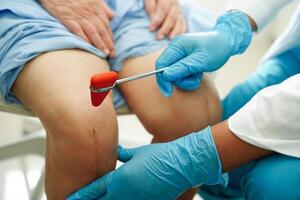asiatique médecin frappe sur le genou réflexe nerf pour vérifier et traitement Sénior patient dans hôpital. photo