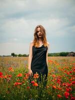 magnifique Jeune fille dans une noir soir robe posant contre une coquelicot champ sur une nuageux été journée. portrait de une femelle modèle en plein air. pluvieux temps. gris des nuages. photo