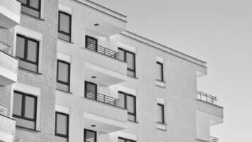 fragment de une façade de une bâtiment avec les fenêtres et balcons. moderne appartement bâtiments sur une ensoleillé journée. façade de une moderne appartement bâtiment. noir et blanche. photo