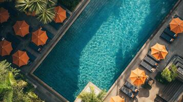 aérien vue de une luxueux Hôtel nager bassin avec pétillant eau, entouré par Orange parapluies et Soleil transats, idéal pour Voyage et été vacances thèmes photo