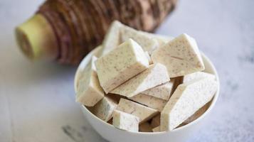 racine de taro avec des cubes de tranche sur bol et fond sombre, racine de taro biologique crue fraîche prête à cuire photo