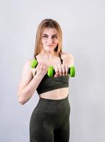 jeune femme sportive faisant des exercices avec des haltères isolés sur fond gris photo