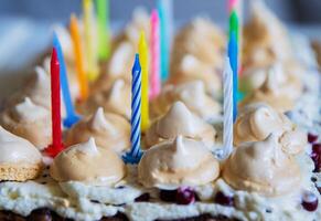 anniversaire gâteau avec blanc fouetté crème, meringues et canneberges, décoré avec multicolore allumé bougies. content anniversaire concept. tradition de fabrication une souhait soufflant en dehors bougies. sélectif se concentrer. photo