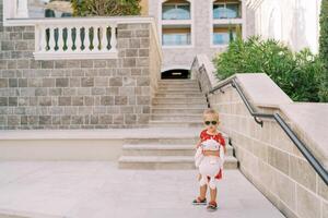 peu fille avec une rose jouet lièvre des stands près le escaliers de un appartement bâtiment dans le jardin photo