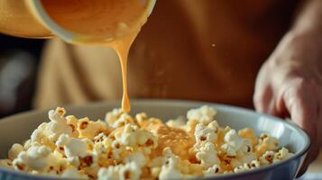 une la personne verser une délicieux et crémeux fondu fromage sauce plus de une bol de classique beurré pop corn création une l'eau à la bouche indulgence photo