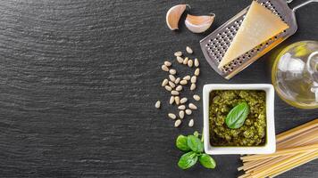 fait maison Pesto sauce dans petit blanc carré pot et Ingrédients pour Pâtes sur noir ardoise Contexte photo