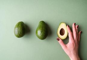 main de femme tenant une moitié d'avocat sur la vue de dessus de fond vert photo