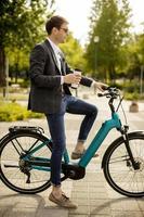 jeune homme d'affaires sur le vélo électrique avec une tasse de café à emporter photo