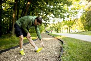 jeune homme athlétique ayant une pause tout en faisant de l'exercice dans un parc verdoyant ensoleillé photo