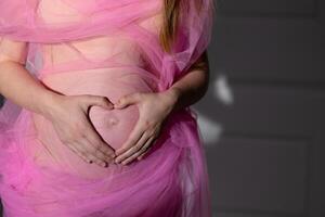 fermer ventre Enceinte rose transparent en tissu les doigts plié comme cœur estomac concept content maternité préparation photo