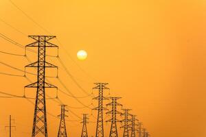 électricité piliers contre une coloré Jaune le coucher du soleil. silhouette haute Tension électrique tours, Puissance lignes. photo