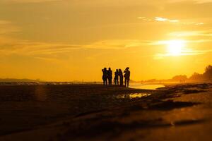 silhouette de une groupe de copains profiter le le coucher du soleil sur le plage à d'or le coucher du soleil temps, relaxant sur une relaxant vacances, mer dans le soir. photo