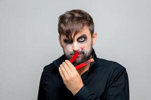 une barbu homme avec Mort-vivant maquillage pour Halloween détient tester tubes dans lequel rouge liquide photo