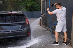 le voitures à une voiture laver courir par une homme avec une l'eau canon. une voiture à une soi un service voiture laver. photo