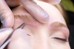 macro la photographie de le posé les sourcils avec le Aidez-moi de laminage, le Maître pince à épiler cueillir le contour de le les sourcils de excès Cheveux photo