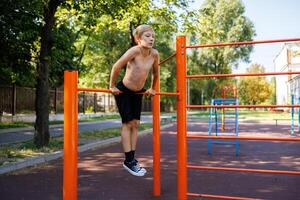 une adolescent détient sa poids sur sa tendu bras tandis que performant éléments sur le bar.rue faire des exercices sur une horizontal bar dans le école parc. photo