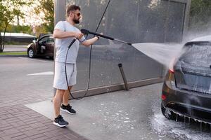 une homme lavages de mousse avec une l'eau canon à une voiture laver. une voiture à une soi un service voiture laver. photo