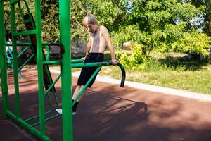 un athlétique enfant effectue des pompes sur le athlétique barres. rue faire des exercices sur une horizontal bar dans le école parc. photo