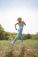 bas vue de un athlétique fille le jogging dans le parc. magnifique blond caucasien femme dans bleu serré survêtement. blond fille à un Extérieur formation session photo