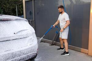 le arrière de le voiture est couvert avec mousse, le homme dans le Contexte est appliquant mousse à le auto. une voiture à une soi un service voiture laver. photo