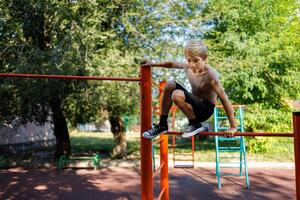 athlétique adolescent veut à sauter de le Haut de le bar. rue faire des exercices sur une horizontal bar dans le école parc. photo