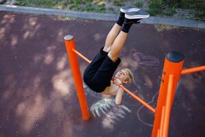 une adolescent exécuté un élément avec élevage jambes par une horizontal bar. rue faire des exercices sur une horizontal bar dans le école parc. photo