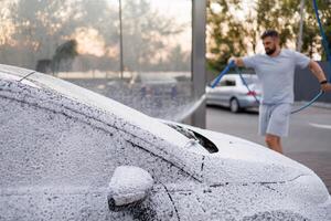 le capuche et pare-brise de le voiture sont couvert avec mousse, le homme dans le Contexte est appliquant mousse à le auto. une voiture à une soi un service voiture laver. photo