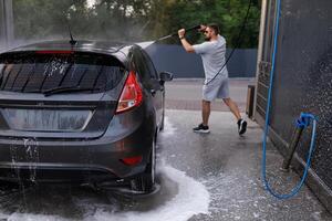 le voiture à le voiture laver, lequel dans le Contexte est lavé avec une l'eau canon par une homme. une voiture à une soi un service voiture laver. photo