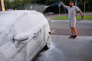 côté vue de une voiture couvert dans mousse, homme dans le Contexte appliquant mousse à le auto. une voiture à une soi un service voiture laver. photo