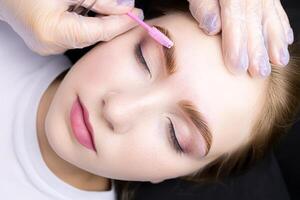 le Maître peignes le les sourcils avec une brosse après le procédure de laminage et sourcil coloration photo