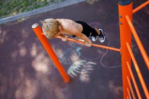 des sports adolescent sur le horizontal bar effectue acrobatique des exercices. rue faire des exercices sur une horizontal bar dans le école parc. photo