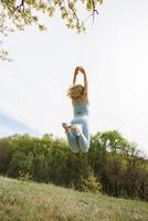 bas vue de une fille athlète sauter dans le Contexte de le parc. magnifique blond caucasien femme dans bleu serré survêtement. blond fille à un Extérieur formation session photo