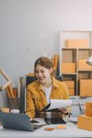 les femmes d'affaires de PME asiatiques utilisent un ordinateur portable pour vérifier les boîtes d'expédition en ligne des commandes des clients à la maison. démarrage d'une petite entreprise entrepreneur PME indépendant. entreprise en ligne, concept de travail à domicile. photo