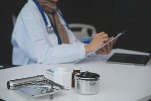 une professionnel et concentré asiatique femelle médecin dans gommages est travail et en train de lire médical recherche sur sa portable dans sa Bureau à une hôpital. photo