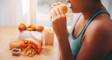 frénésie en mangeant désordre concept avec femme en mangeant vite nourriture Burger, mis à la porte poulet , beignets et desserts photo