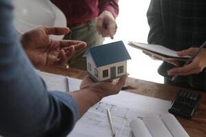 ingénieurs sont consultant le équipe à conception un architectural structure pour clients avec plans et bâtiment des modèles à travail à bureau. photo