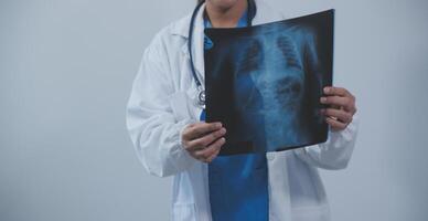 asiatique musulman médecin dans hijab et gommages écouteurs autour sa cou supporter en toute confiance dans le médical bureau, isolé sur blanc arrière-plan, en portant radiographie film. photo