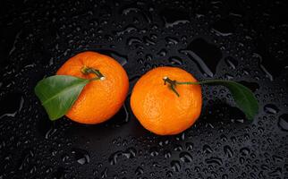 deux mûr juteux mandarines sur une noir Contexte avec gouttes de l'eau. photo