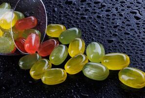 une lot de bonbons cannes sont épars de un renversé verre gobelet. multicolore des sucreries dans une verre sur une noir Contexte. confiture des sucreries. photo