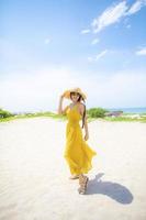 Belle femme asiatique portant des vêtements jaunes debout sur la plage de la mer contre la lumière du soleil de midi