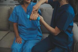 vieux femme formation avec physiothérapeute en utilisant haltères à maison. thérapeute assistant Sénior femme avec des exercices dans allaitement maison. personnes âgées patient en utilisant haltères avec tendu bras. photo