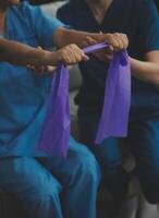 personnel entraîneur assistant Sénior femme avec la résistance groupe. réhabilitation physiothérapie ouvrier portion vieux patient à allaitement maison. vieux femme avec étendue bande étant coaché par physiothérapeute. photo